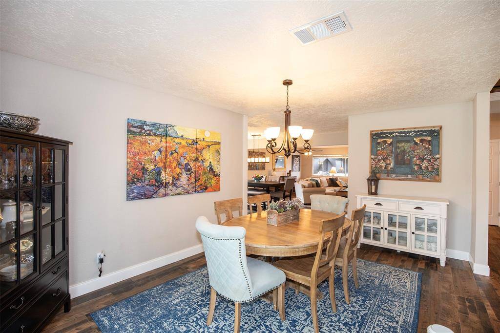 This inviting dining area features a large window with plenty of natural light, a stylish chandelier, and wood flooring. The space is enhanced with loads of natural light and opens to a modern kitchen with white cabinetry.