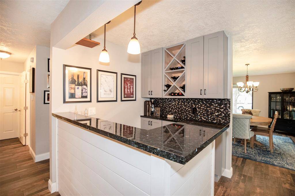 This kitchen features modern stainless steel appliances, sleek black granite countertops, and white cabinetry. It has a stylish tile backsplash, hardwood floors, and ample natural light from a large window, creating a bright and inviting space.