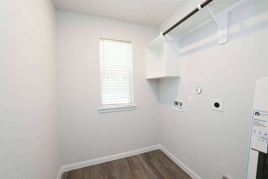 This photo showcases a compact, well-lit laundry room with a window, hookups for a washer and dryer, and a shelf with a hanging rod for storage.