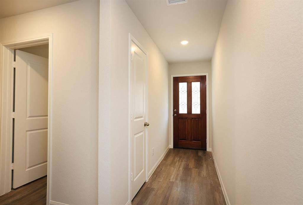 The bright, narrow hallway Entry with light-colored walls and vinyl plank flooring includes two doors on the left side, providing additional access to rooms.