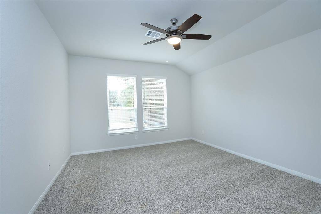 The soft gray walls, plush carpet, and ample natural light from two windows with blinds creates a lovely sanctuary for the Primary Bedroom. A ceiling fan is centrally located, providing a modern touch and functional airflow.