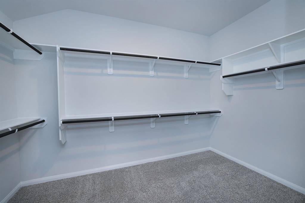 Am I right? A spacious walk-in closet with multiple shelves and hanging rods, featuring neutral walls and carpet flooring make for an ideally organized storage spot.