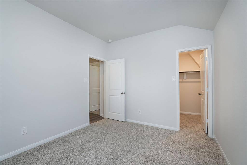 The walk-in closet provides ample storage and an open door leads to a hallway. The room is well-lit and has a simple, clean design.