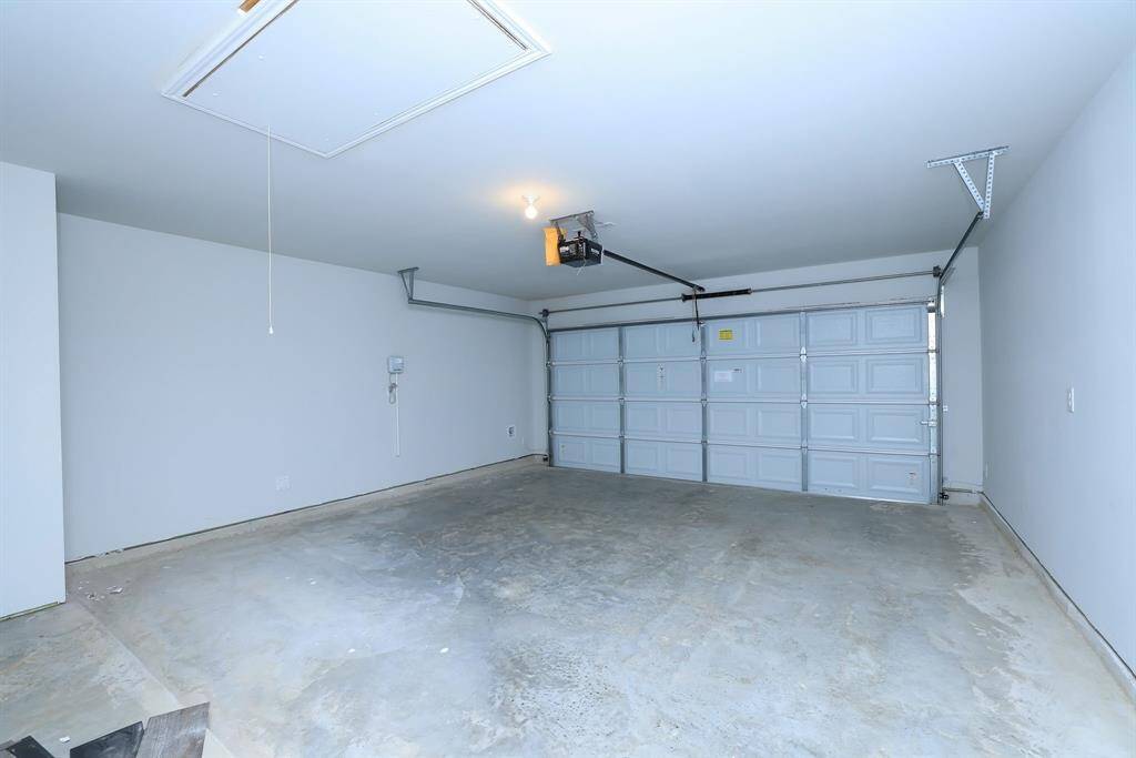 The two-car garage features a concrete floor, white walls, and a large automatic door. It's well-lit and offers ample storage or parking space. The concrete pad could also house a secondary refrigerator.