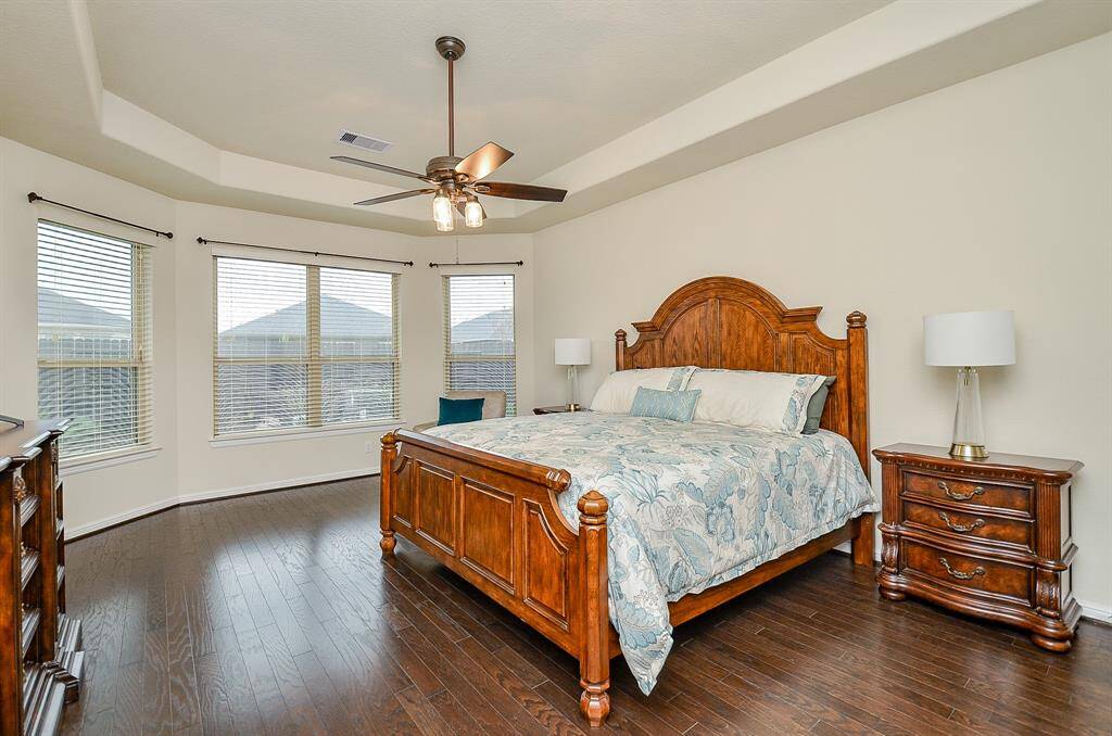 The primary suite is a true retreat, featuring a high tray ceiling with a stylish fan that adds to its elegance. Gleaming wood floors enhance the room's warmth, while a large bay window invites abundant natural light, creating a bright and serene atmosphere.