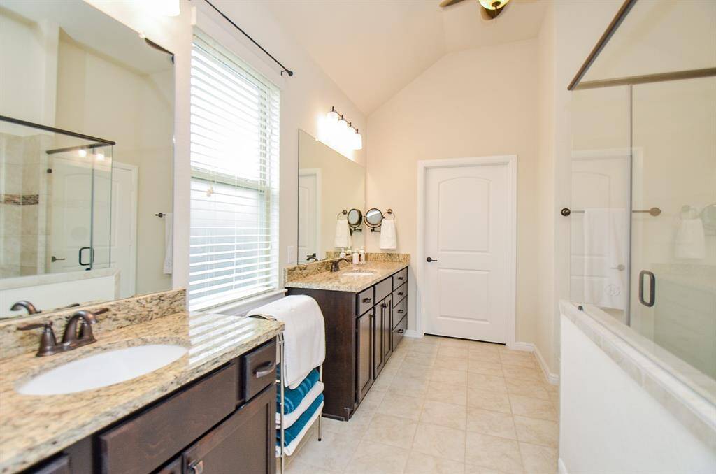 The luxurious ensuite bathroom offers dual vanities with sleek granite countertops, complemented by large frameless mirrors and updated vanity lighting, creating a polished and spa-like atmosphere.