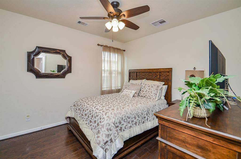 The secondary bedroom is thoughtfully designed, offering ample space and comfort for family or guests. With a high ceiling and fan, gleaming wood floors, and a large window that fills the room with natural light, it provides a welcoming and relaxing retreat.