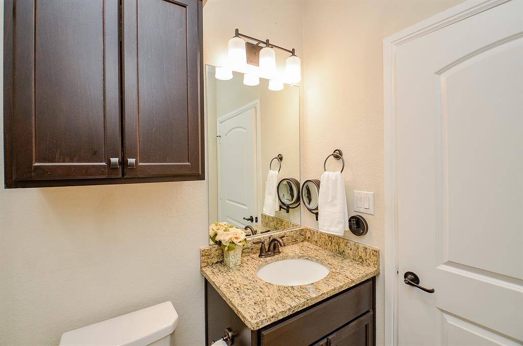 This full secondary bathroom features a granite-topped vanity with a frameless mirror and overhead vanity lighting.