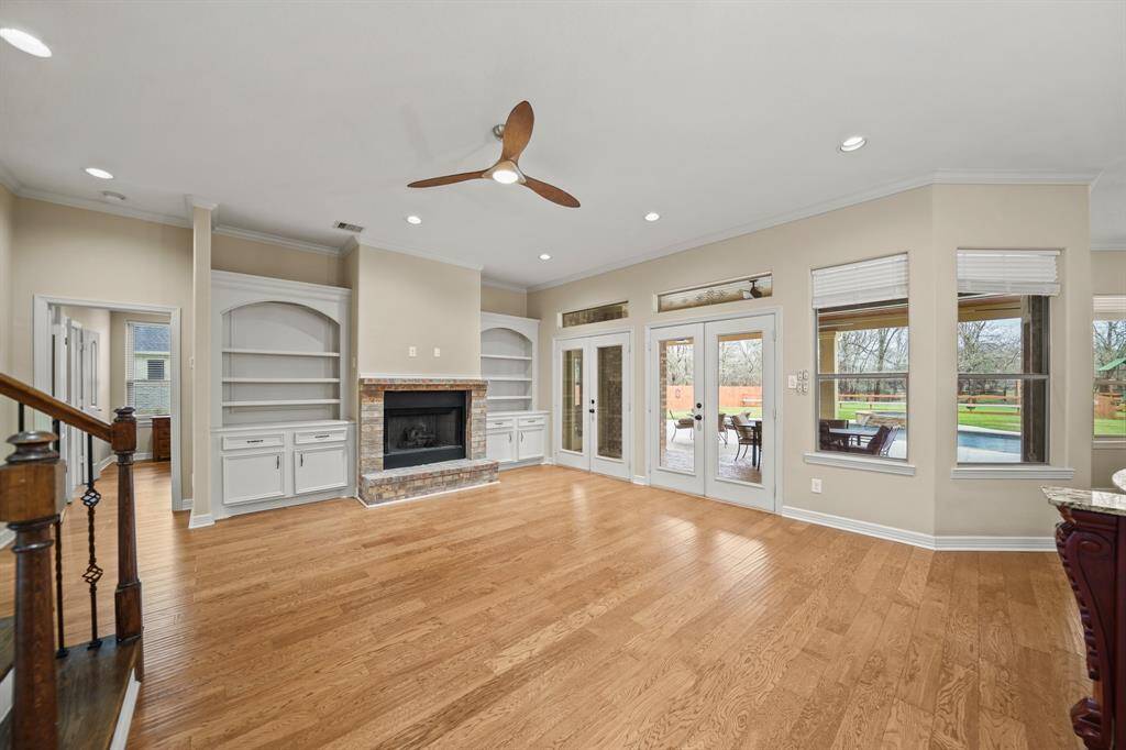 The spacious family room centered around a striking fireplace with custom built-ins on either side. Two glass French doors open to the outdoors, while a rich wood staircase with  wrought iron balusters lead you upstairs.