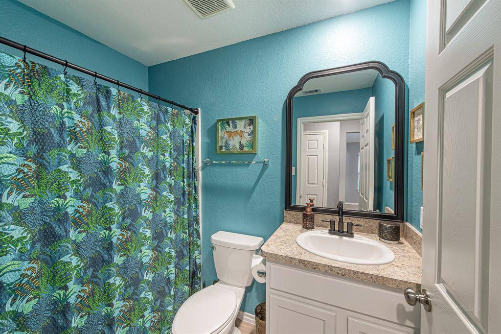 This bathroom features vibrant teal walls and a sleek vanity with a black-framed mirror.
