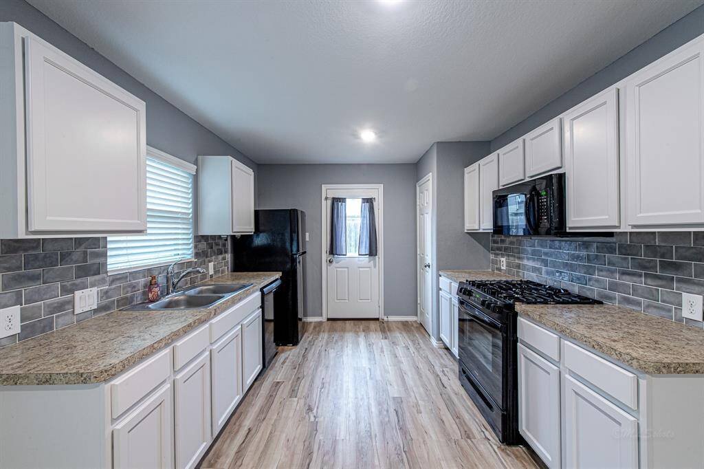 White cabinets, 5-burner gas range, black appliances, and fridge included.