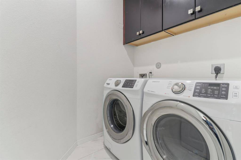 This photo shows a laundry room with complemented by upper storage cabinets.