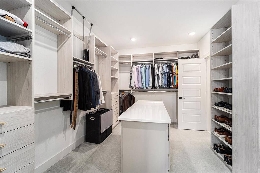 Expansive primary closet featuring custom built-ins throughout, including a central island with drawers for additional storage, offering ample space and organization.