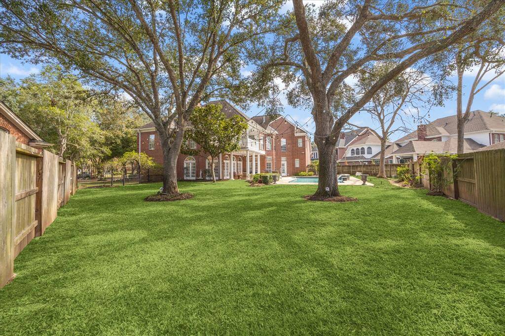 A large grassy green space to the left of the pool for running and playing. Large established trees. All fenced. Premium oversized lot.