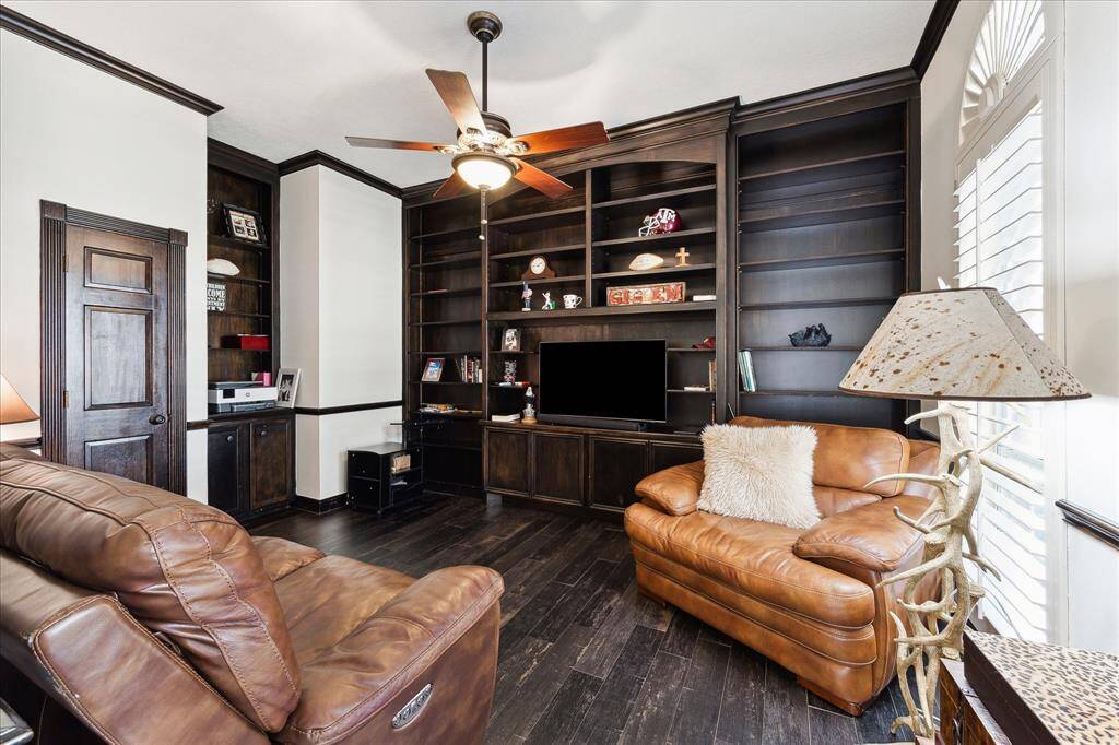 Study has rich, stained hardwood flooring, built-in book shelves, and plantation shutter with a sunburst topper.