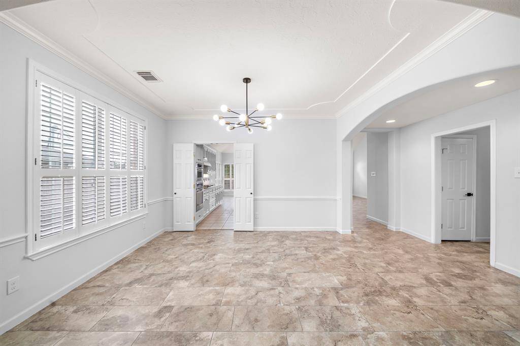 Bright and inviting, the formal dining area showcases updated modern lighting, elegant architectural details, and large windows with plantation shutters that fill the space with natural light.