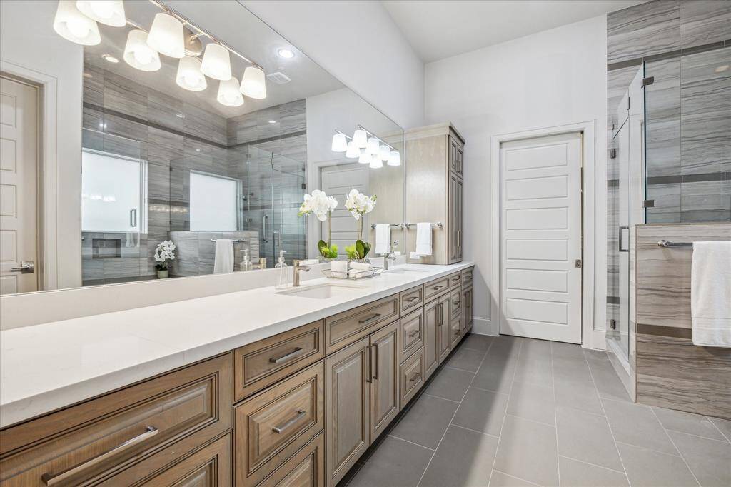 PRIMARY BATHROOM: The primary bathroom is a true sanctuary, where luxury and serenity come together seamlessly. The expansive vanity boasts dual sinks, framed by custom-stained cabinetry and adorned with elegant stone countertops.