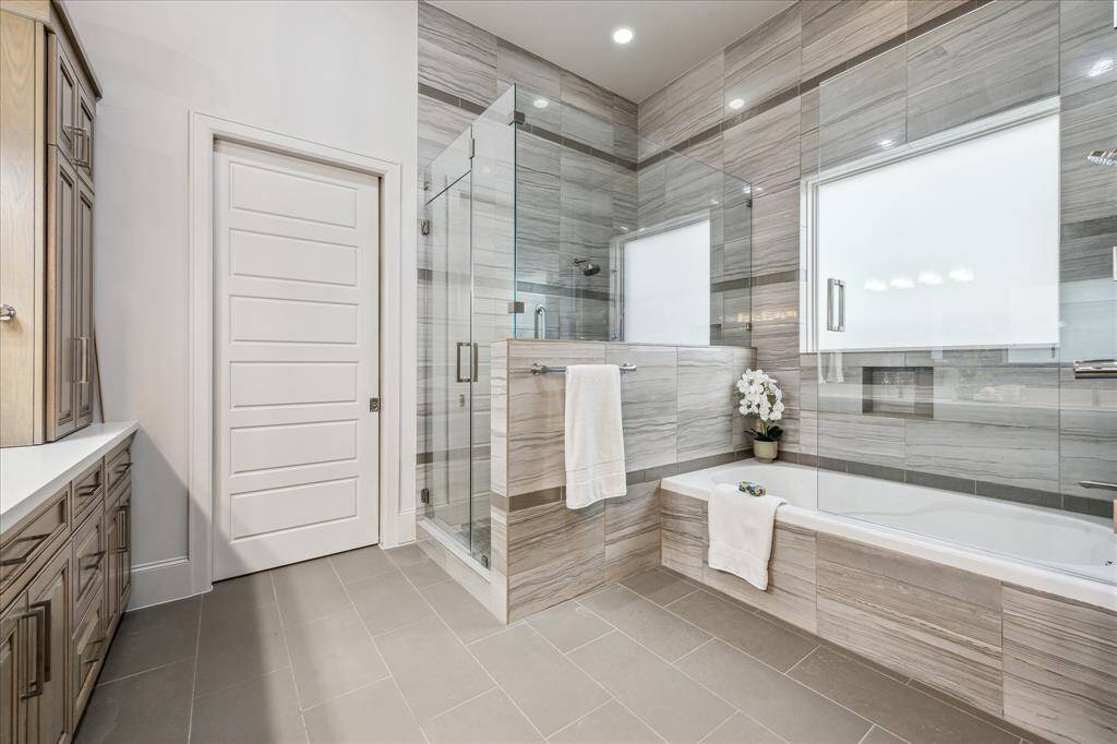 PRIMARY BATHROOM: Spa-like soaking tub invites tranquility, surrounded by stunning tiles that elegantly wrap the walls, creating a cohesive, serene atmosphere. The walk-in shower is equally impressive, with gorgeous tiles extending from floor to ceiling, adding a sense of seamless beauty. Every detail, from the exquisite finishes to the thoughtful design, transforms this space into an indulgent escape!