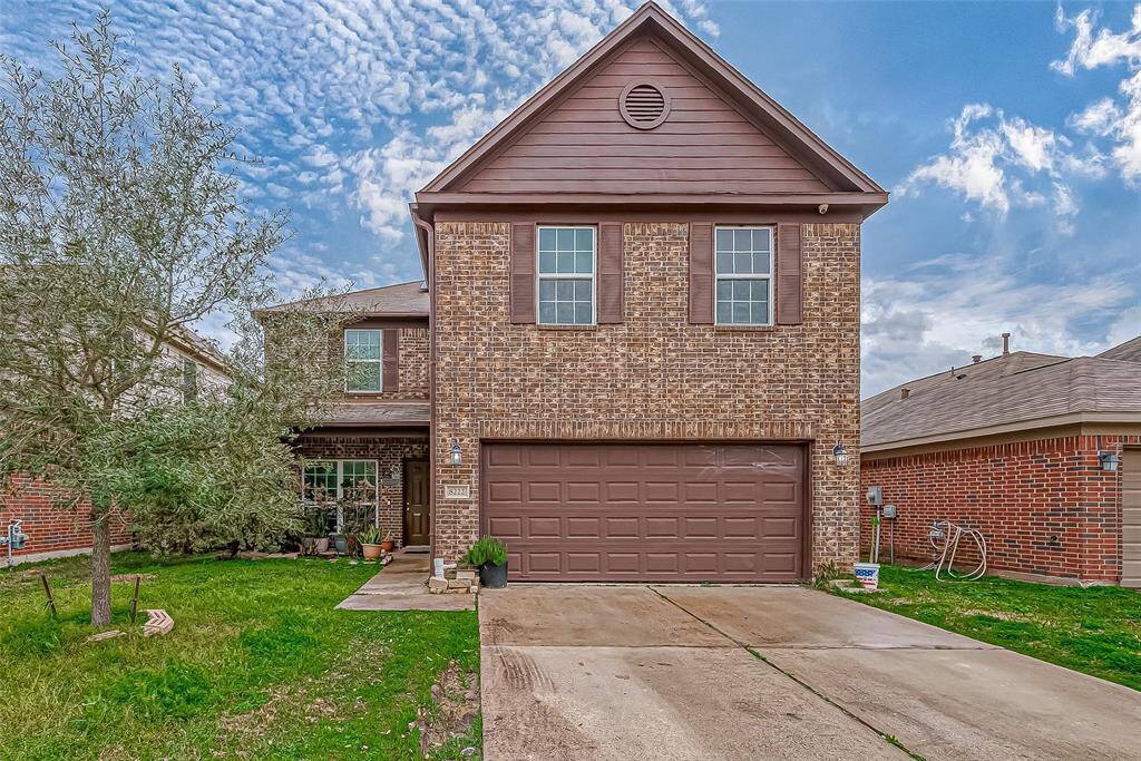 A striking facade of rich, dark brick rises tall, framed by a well-manicured lawn. The broad driveway, neatly paved, leads to a two-car garage, providing ample space for parking and storage.