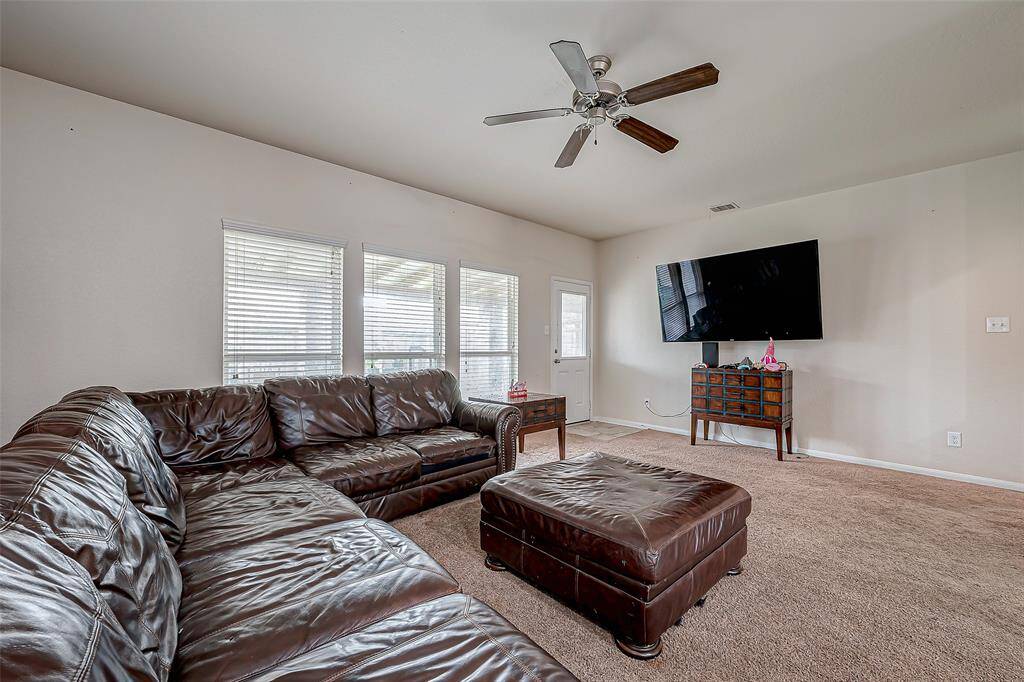An impressive gathering space, the living room stretches out with abundant square footage, easily accommodating a variety of seating arrangements. Multiple large windows flood the space with light, while the neutral walls and plush carpeting create a soft, inviting ambiance. A door leads directly to the backyard, extending the living space outdoors.
