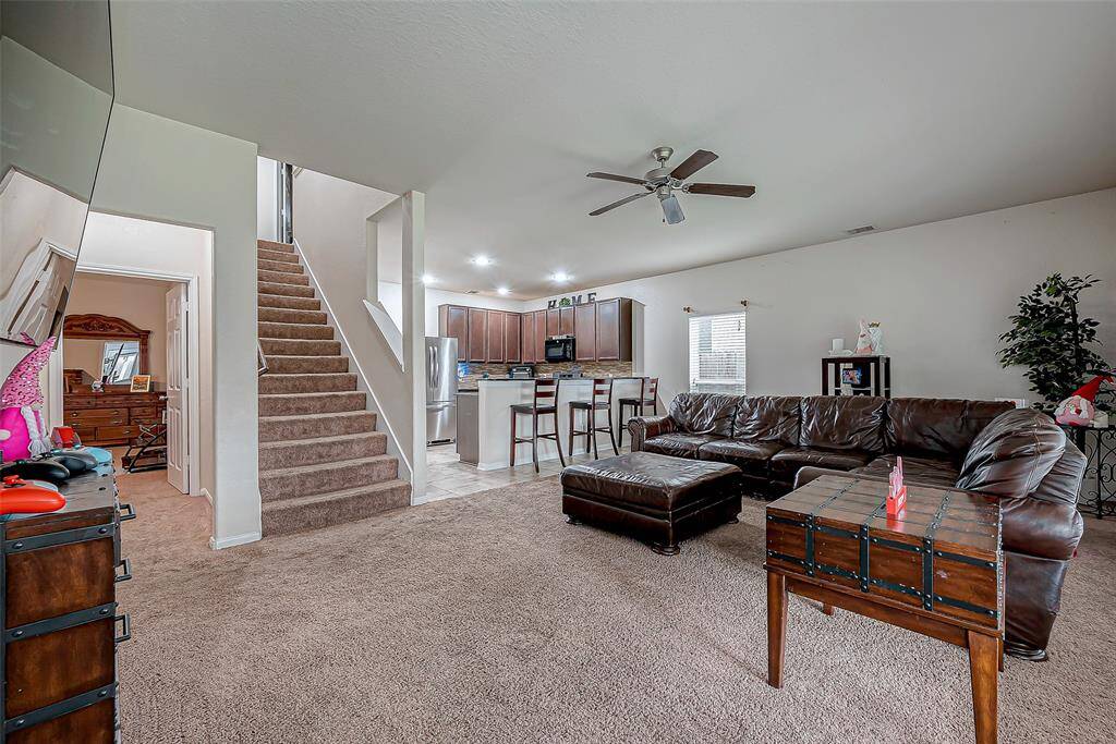 The staircase in view adds a striking visual element, while the ceiling fan and expansive carpeting enhance the room’s comfort.
