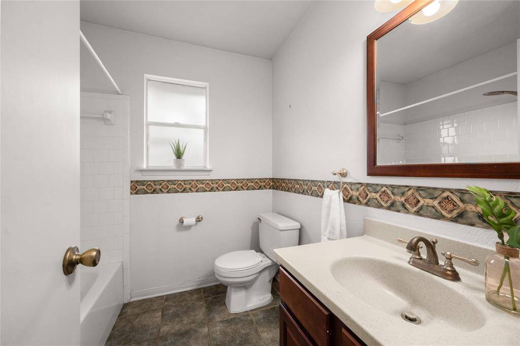 This inviting secondary bathroom is a welcome retreat for family or guests.  It contains a large contemporary mirror, a sparkling white tub/shower tile surround and gorgeous tile flooring that compliment the rich wood grains of the cabinet and mirror and contrast perfectly with the bath tile, walls and counter.