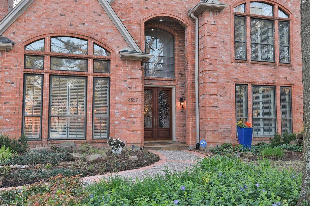 The pebble stone walkway leads to the elegant entry featuring an impressive wood grain door with sculptured glass windows framed by an arched brick patio and a large picture window. Flanked by stylish lanterns, it offers a welcoming and sophisticated first impression.
