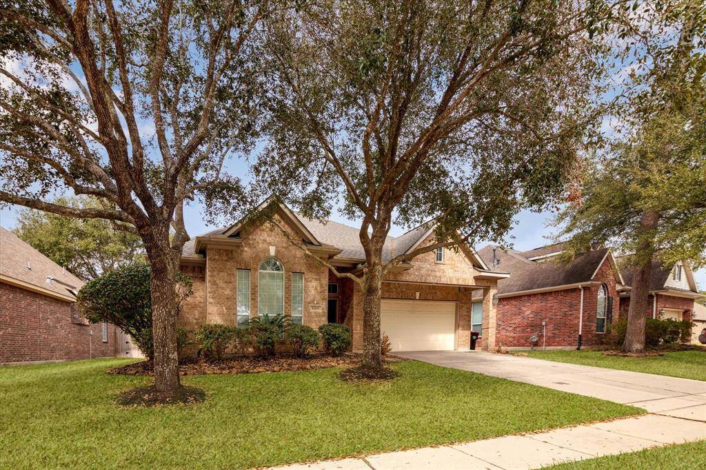 Charming brick home with a welcoming arched window and a two-car garage. It features a well-maintained front yard with mature trees and a spacious driveway, situated in a pleasant neighborhood.