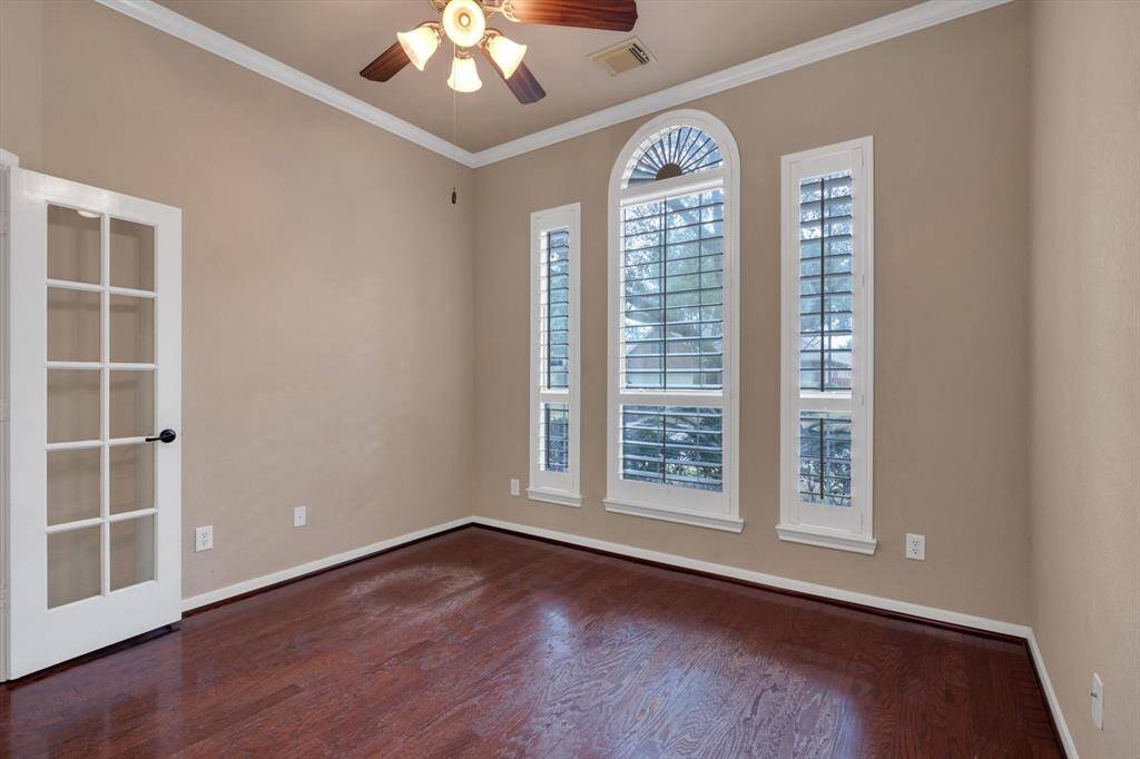 This room features hardwood floors, neutral walls, and a ceiling fan. It has a set of large windows with plantation shutters, allowing natural light. A French door adds elegance and style. Perfect for an office or cozy sitting area.
