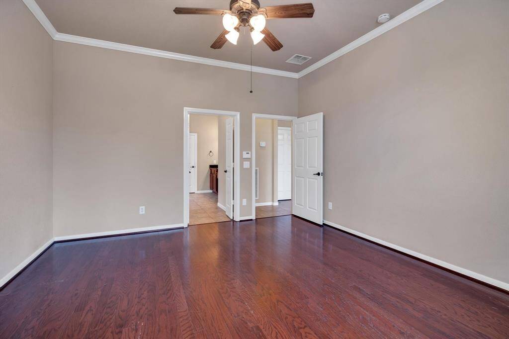 This room features rich hardwood flooring, neutral walls, and a ceiling fan. It has crown molding and two doors leading to adjacent spaces, providing a versatile layout.