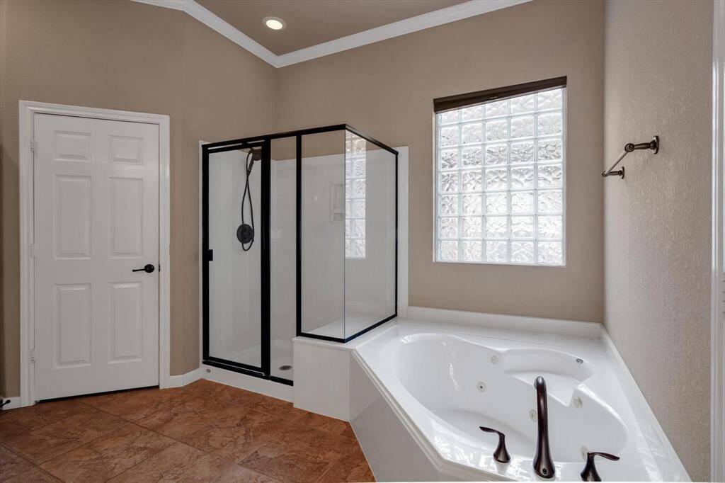 This bathroom features a modern design with a spacious glass-enclosed shower and a corner jacuzzi tub. The room is brightened by a large glass block window, and the neutral tile floor complements the warm wall color.