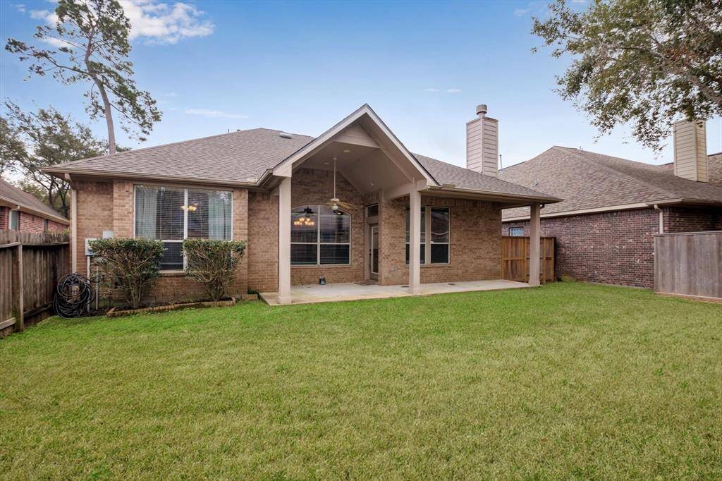 This photo showcases a charming brick home with a covered patio, large windows, and a well-maintained fenced backyard, perfect for outdoor activities and entertaining.