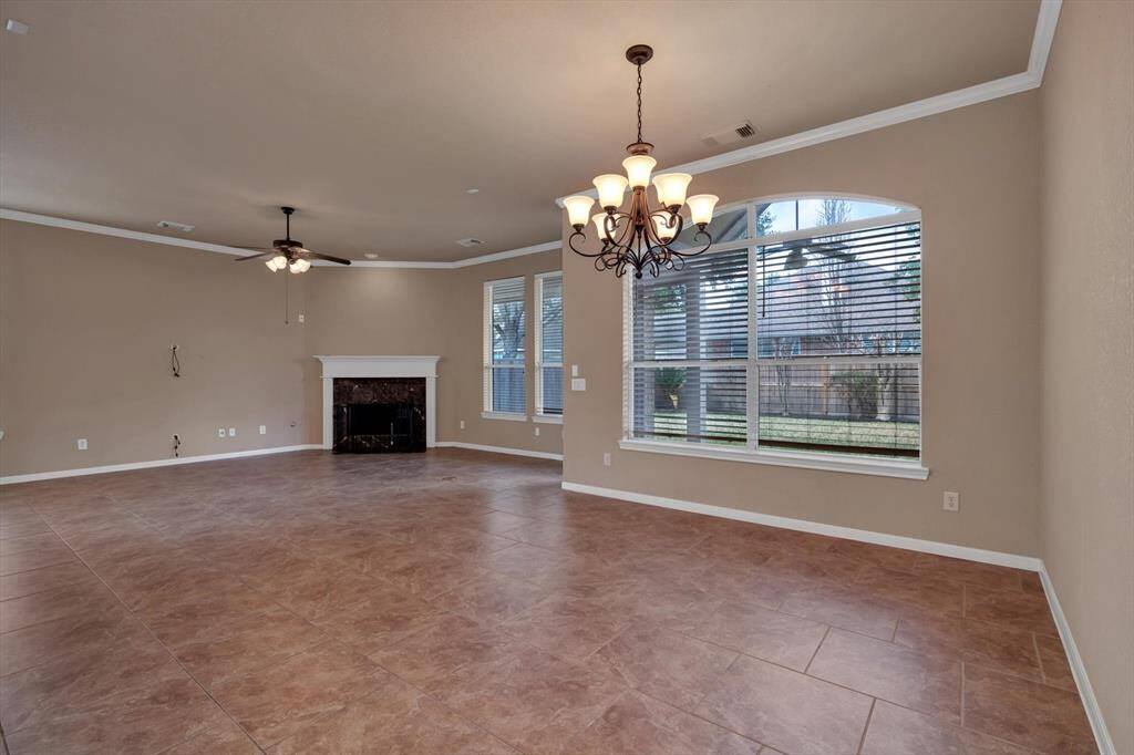 This spacious living area features neutral-toned walls and tile flooring. It includes a cozy fireplace, large windows for natural light, and elegant light fixtures, creating a warm and inviting atmosphere.