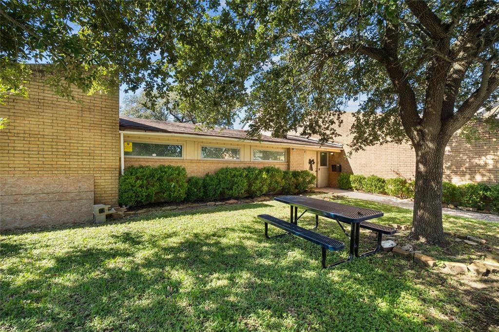 The spacious front yard is enclosed by a white fence. The picnic table sits under a large tree, suggesting a communal outdoor space where you can go to relax or sit in the shade.