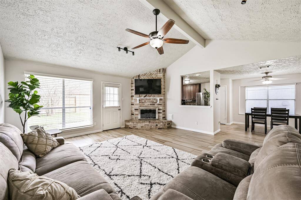 Beautiful living room featuring a vaulted ceiling, neutral paint, a brick fireplace with a mantle, and porcelain flooring. This is a great space for entertaining.