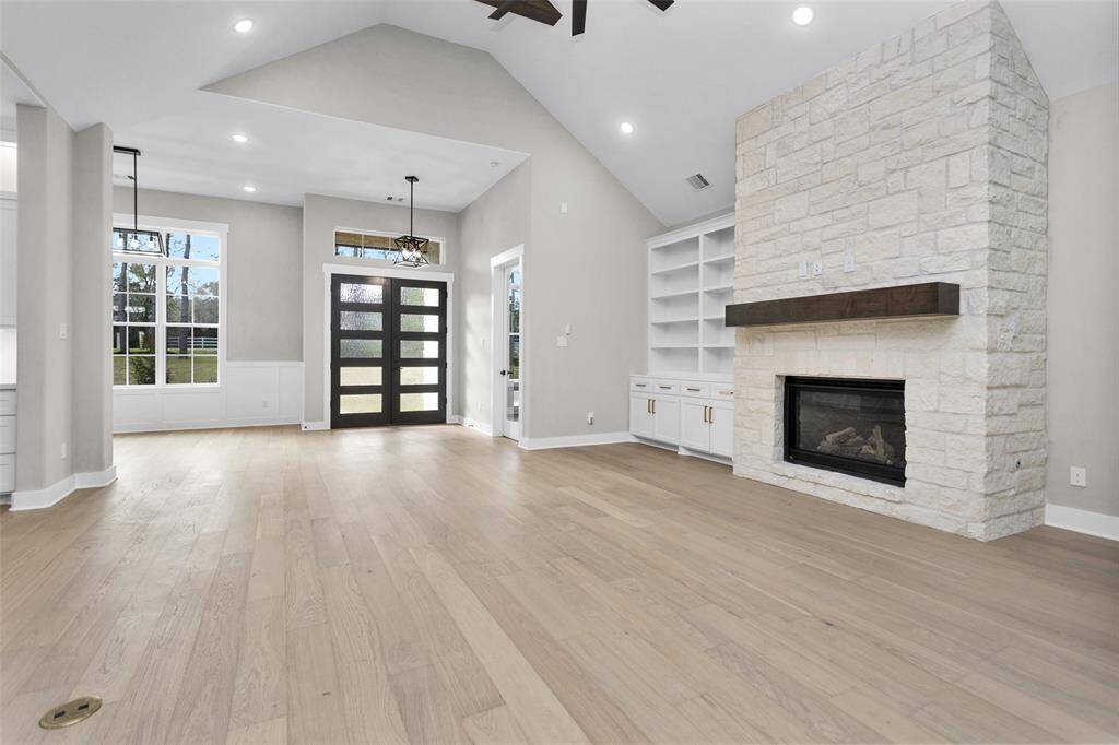 A bright and spacious living room featuring a stone-accented fireplace, large windows, and exposed ceiling beams.