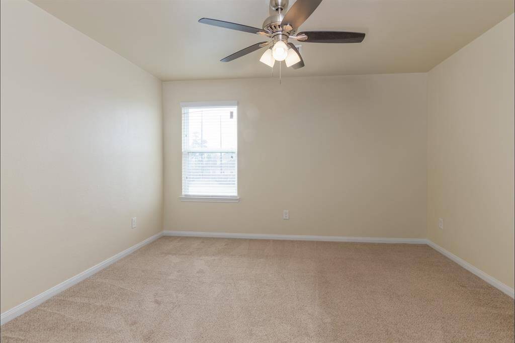 This is a cozy, carpeted room with neutral walls, featuring a ceiling fan and a window that lets in natural light. Ideal for a bedroom or office space.