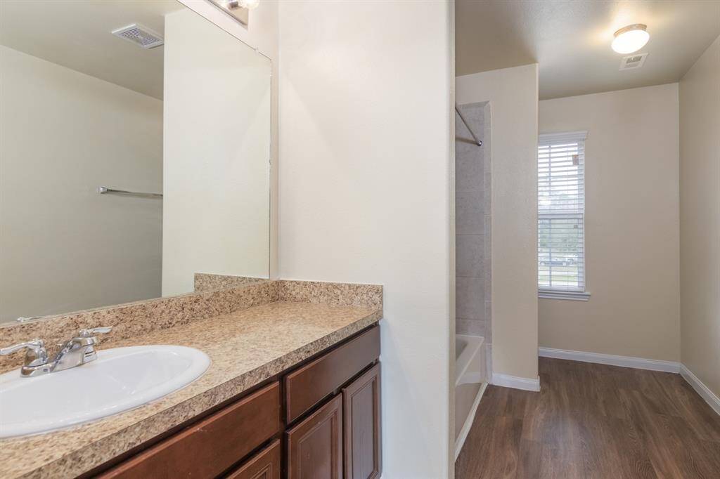 This is the Primary Bathroom which features a sleek design with a granite countertop, under-mount sink, and wooden cabinetry. It includes a tub-shower combo and a window for natural light, complemented by a wood-look floor.