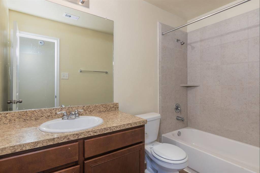 This bathroom features a clean and modern design with a granite countertop, under-mount sink, and a spacious mirror. It includes a bathtub with tiled walls and a built-in shower, combining functionality with style.