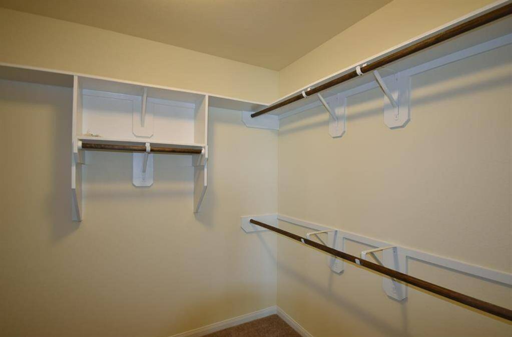 A spacious walk-in closet with multiple wooden hanging rods and built-in shelving, perfect for ample storage. The carpeted floor adds warmth to the space.