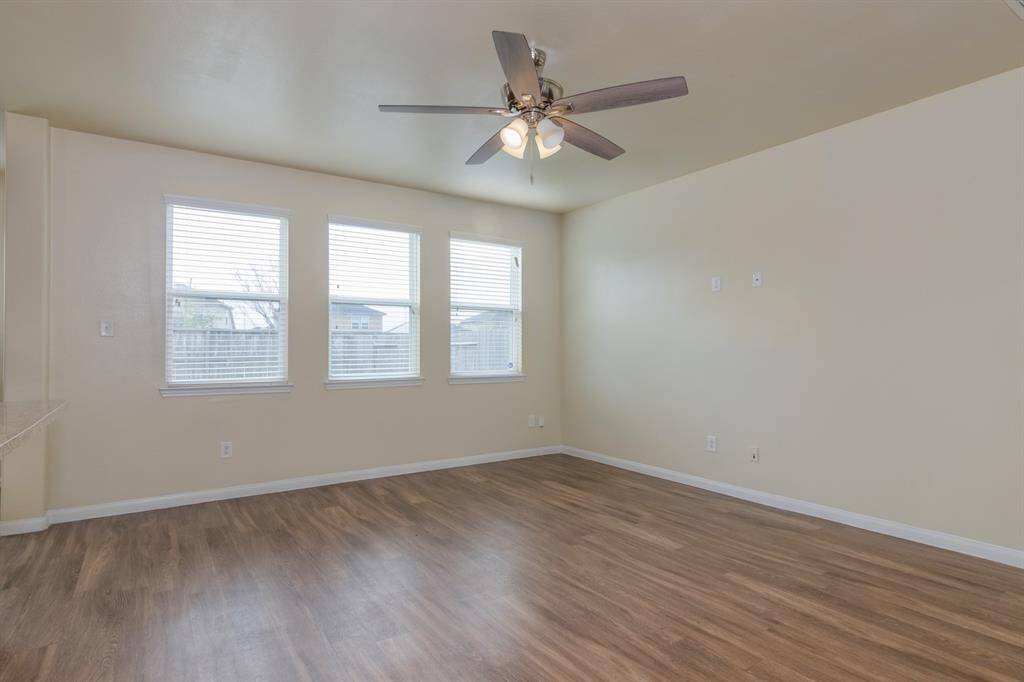 This room features an open, airy layout with three large windows providing ample natural light. It has a modern ceiling fan and wood-look flooring, creating a warm and inviting space.