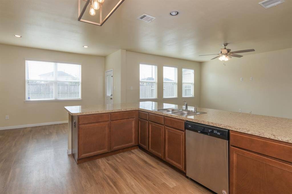 This open-concept kitchen features hardwood floors, ample natural light, and a spacious island with granite countertops. It includes a stainless steel dishwasher and a ceiling fan in the adjoining living area, offering a modern and inviting space for entertaining.