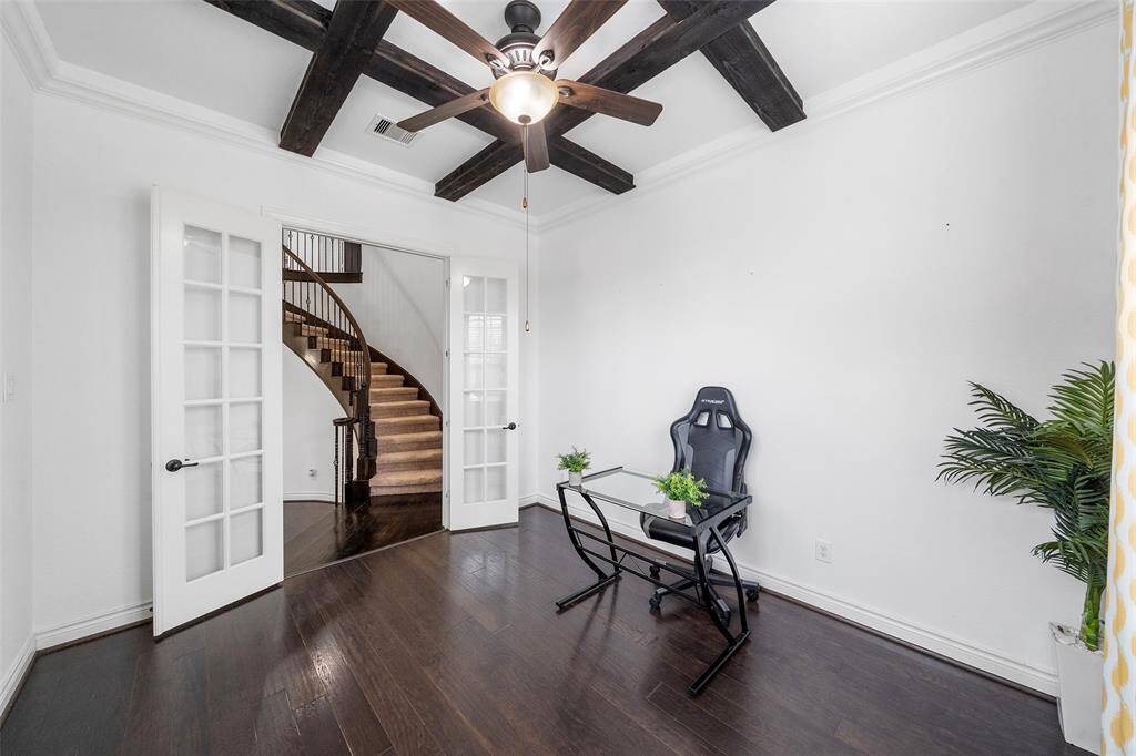 This room features sleek dark wood flooring and exposed ceiling beams, creating a modern yet cozy atmosphere. The space is enhanced by French doors leading to a curved staircase, adding elegance and charm.