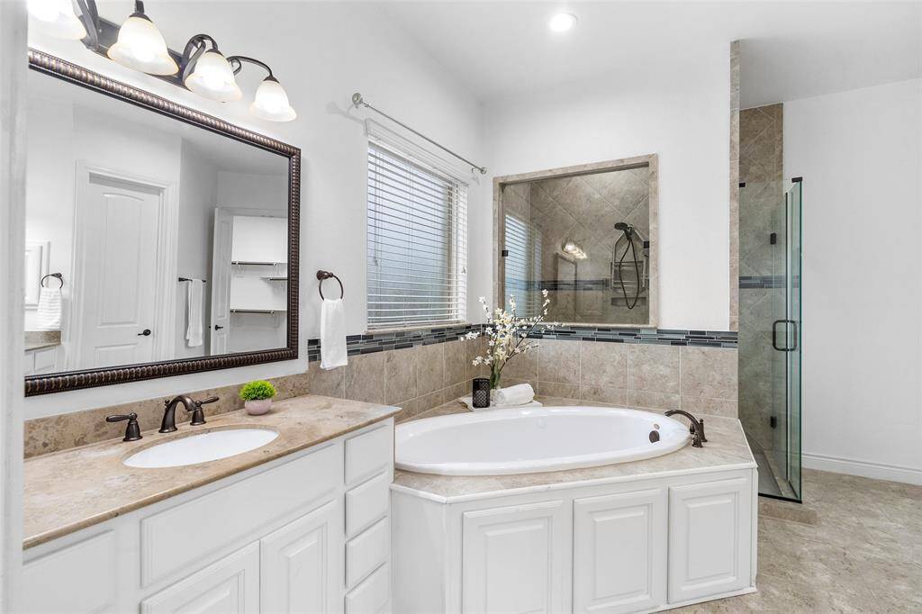 This spacious bathroom features a luxurious soaking tub, a separate glass-enclosed shower, and a large vanity with dual sinks. The modern fixtures and elegant tile work create a relaxing atmosphere.