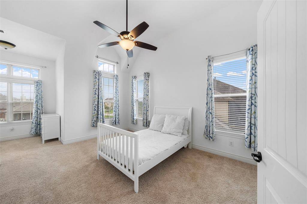 Bright and airy bedroom with high ceilings, carpeted flooring, and ample natural light from multiple windows.