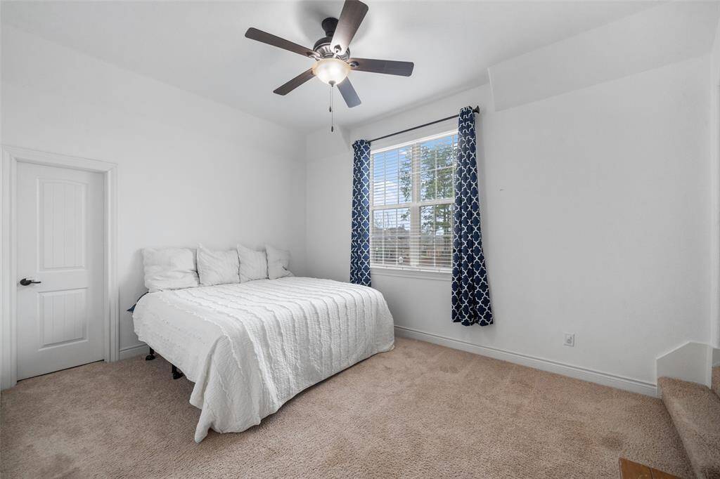 This is a bright, cozy bedroom featuring a large window with blue patterned curtains, a ceiling fan, and a comfortable bed with white bedding. The closet in this bedroom is gigantic for a secondary bedroom.