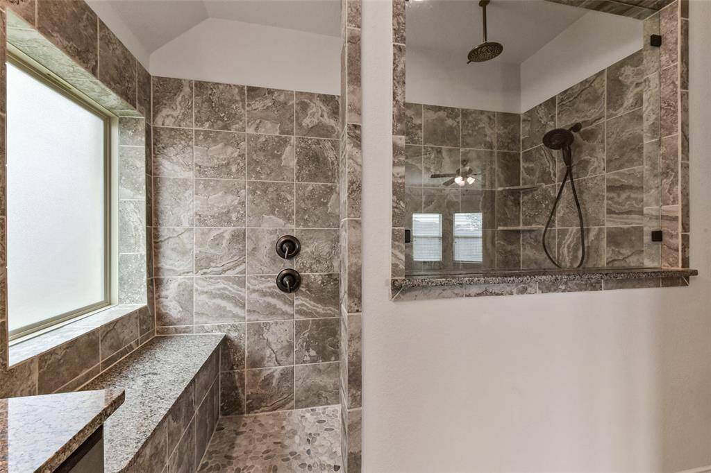 Shower features full tile surround, an extra shower head above, and granite bench. Privacy glass window.
