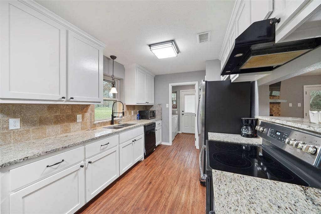 This is a modern kitchen with white cabinetry, granite countertops, stainless steel appliances, and a view into an adjacent dining area with hardwood like floors. There's ample natural light and a window over the sink.