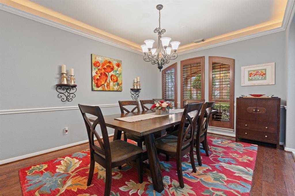 This dining room features elegant crown molding, a stylish chandelier, and warm wooden floors.
