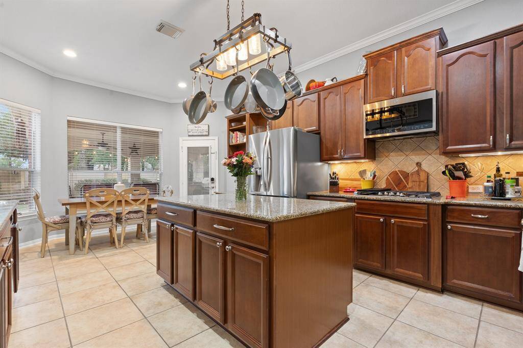 This spacious kitchen features elegant wooden cabinetry, a large center island with granite countertops, and a hanging pot rack.